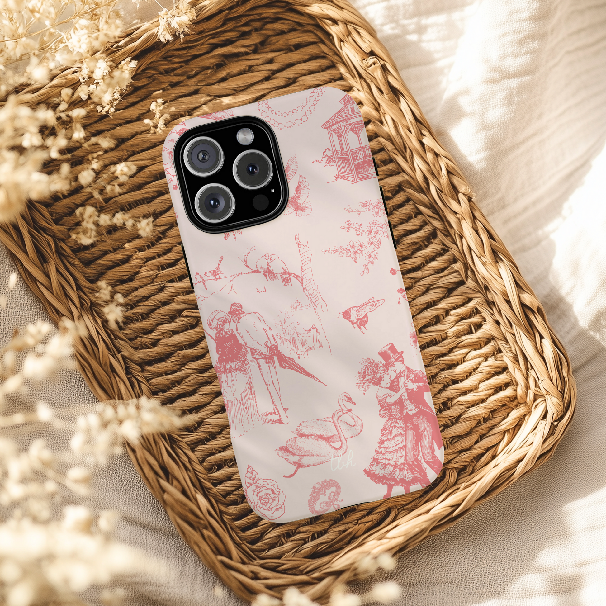 Phone case with pink and white design on a woven tray with dried flowers